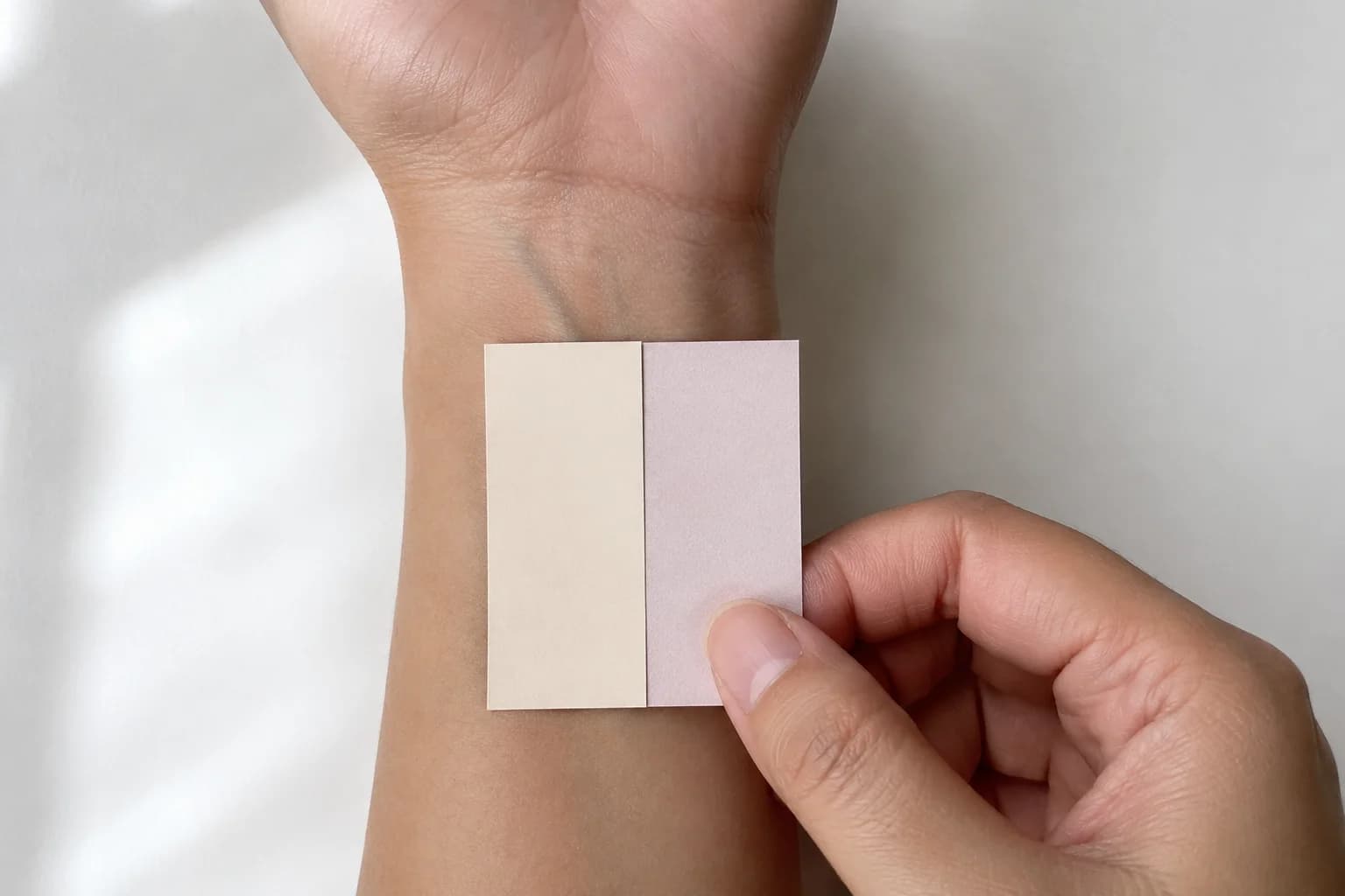 Two color swatches held against an inner wrist to compare warm and cool undertones