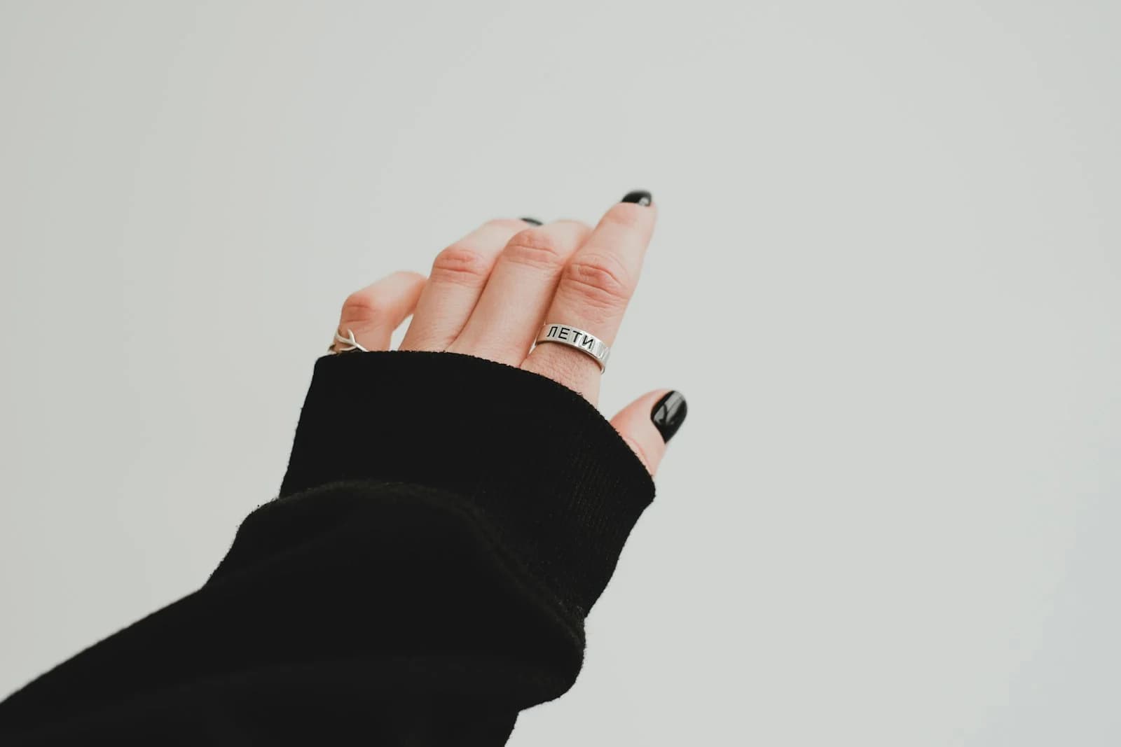 Hand wearing a silver ring against a plain background