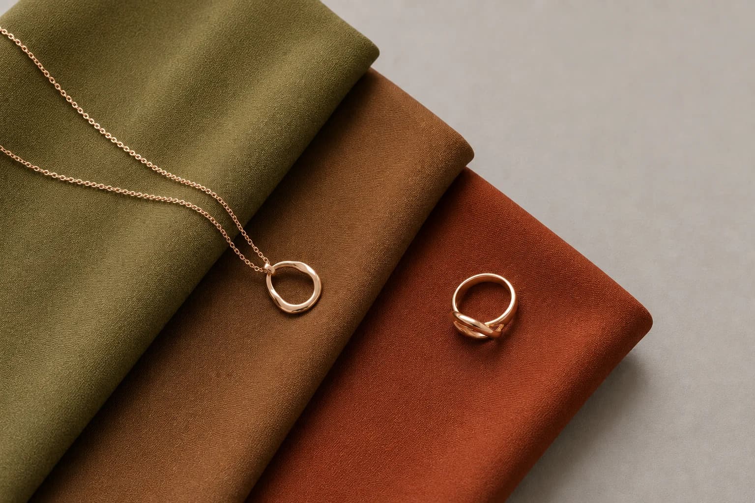 Stoffmuster in Moosgrün, Bronze und Terrakotta mit Roségold-Schmuck, stellvertretend für eine Farbpalette mit olivem Unterton